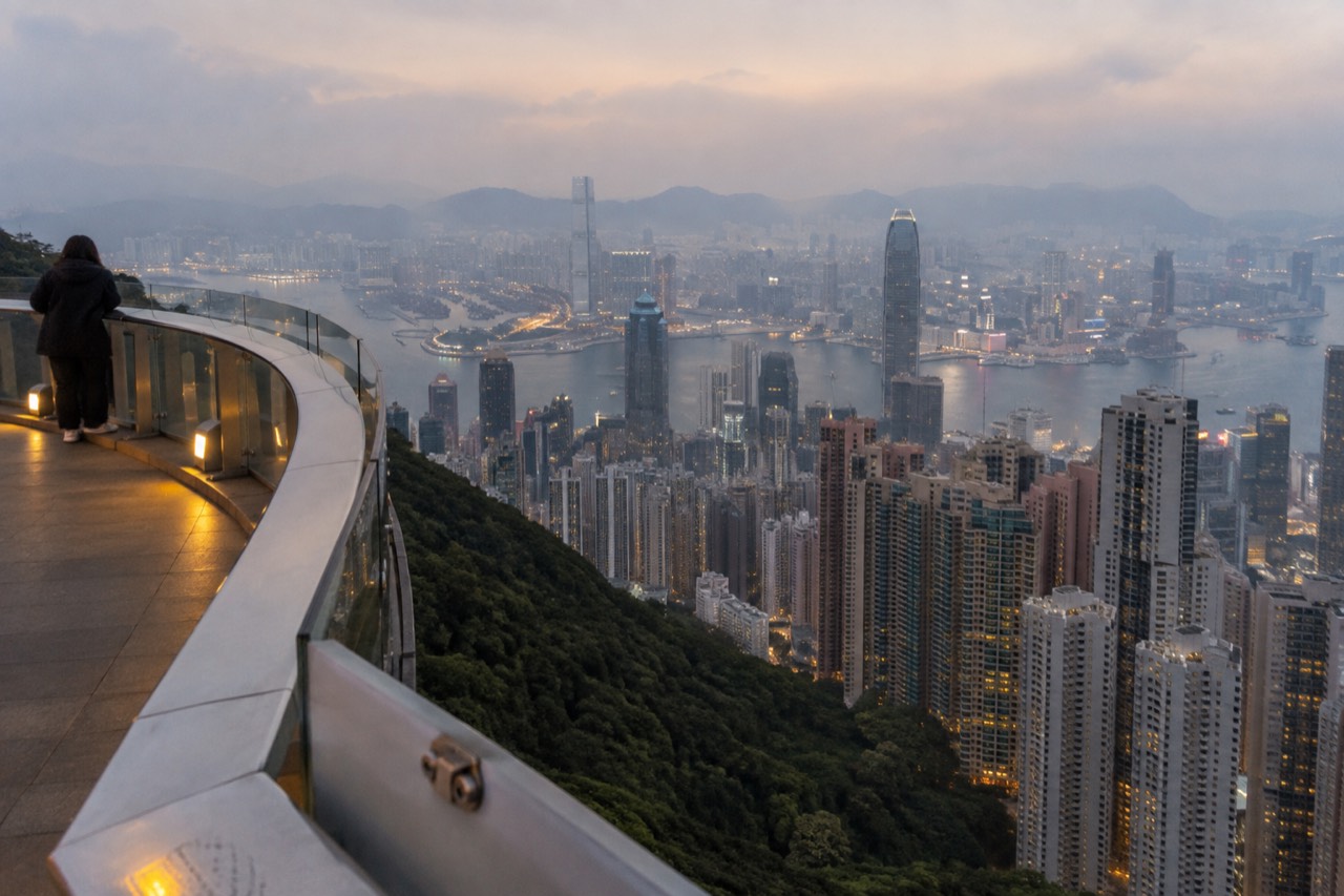 Rooftop observation deck railing overlooking a dense city skyline and harbour at dusk