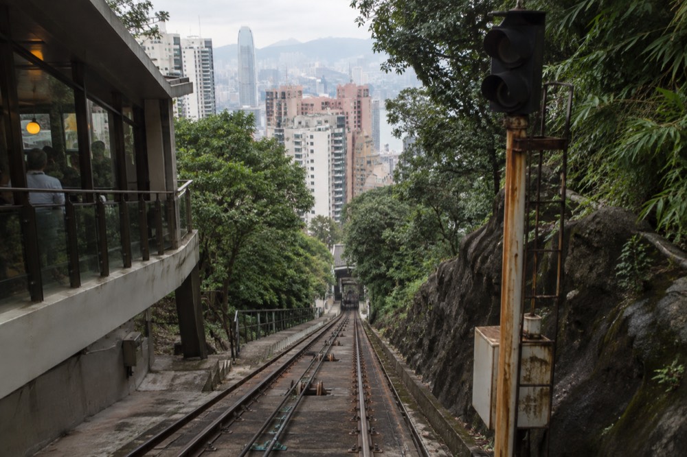Steep funicular track rising through trees with apartment towers visible down the slope