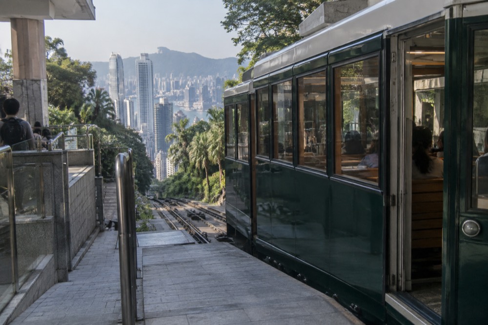 A green funicular tramcar at a hillside station above a city of tall buildings