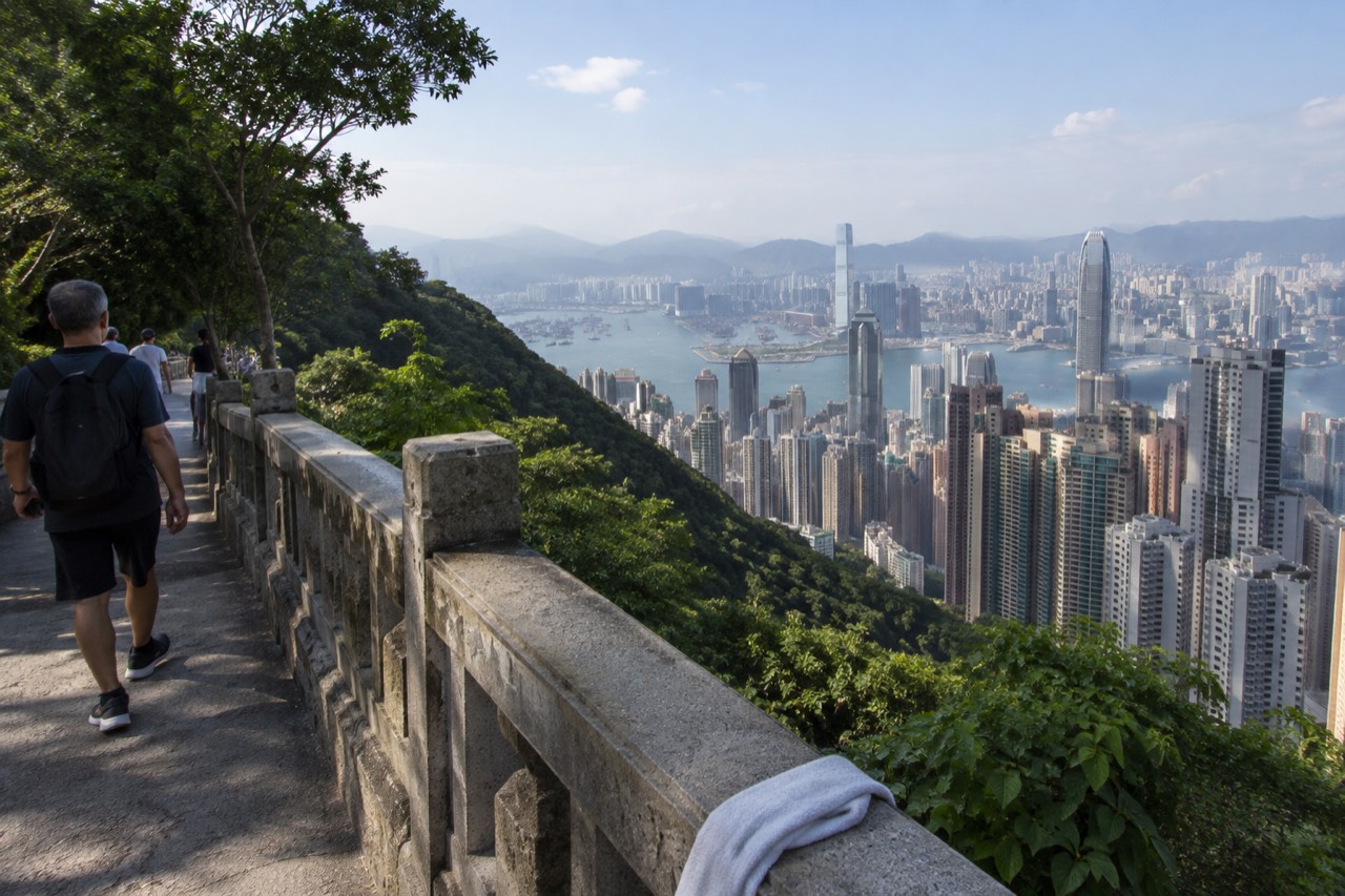 A paved walking path along a green hillside with the Hong Kong skyline and harbour spread out below