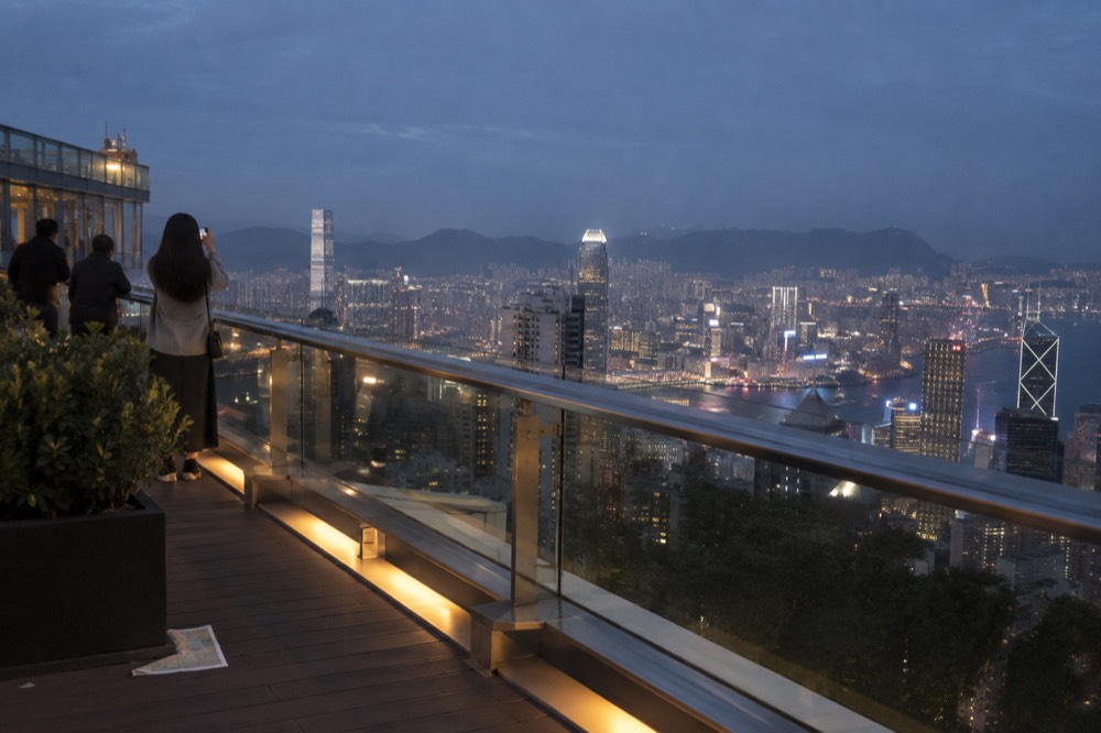 A hilltop observation deck at dusk overlooking a lit harbour city skyline