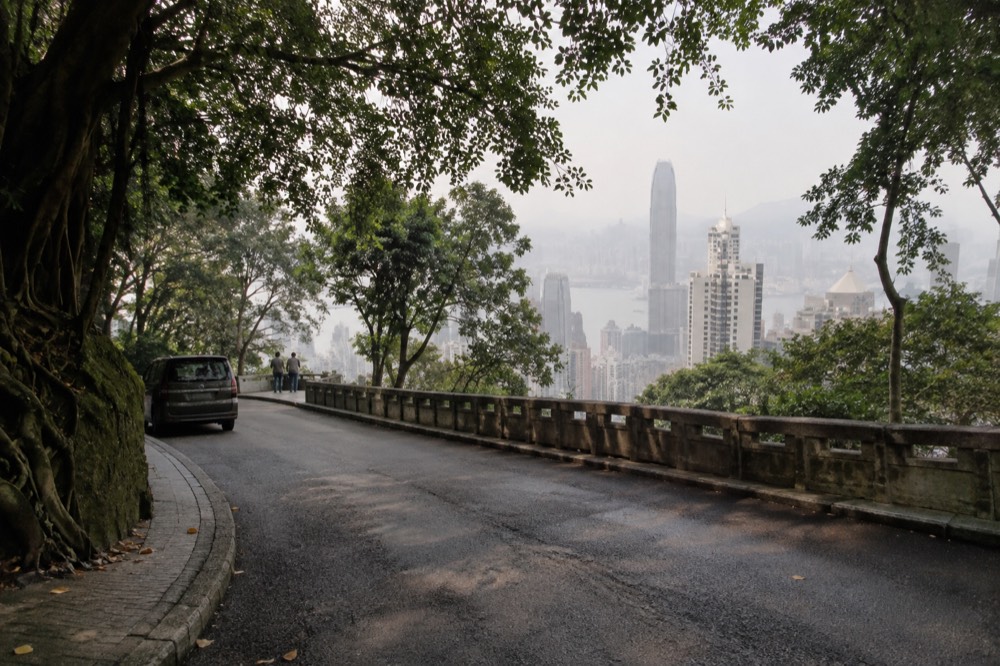 Flat tree-lined section of Lugard Road with apartment towers visible through the trees