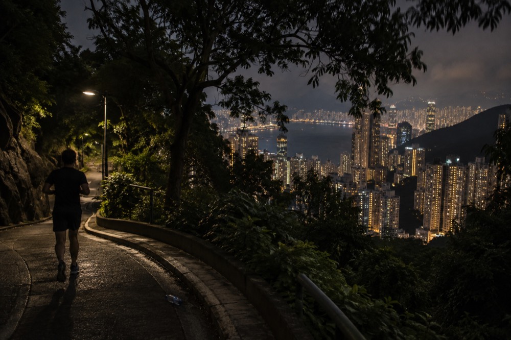 A lit walking path along a hillside road with the city glowing below