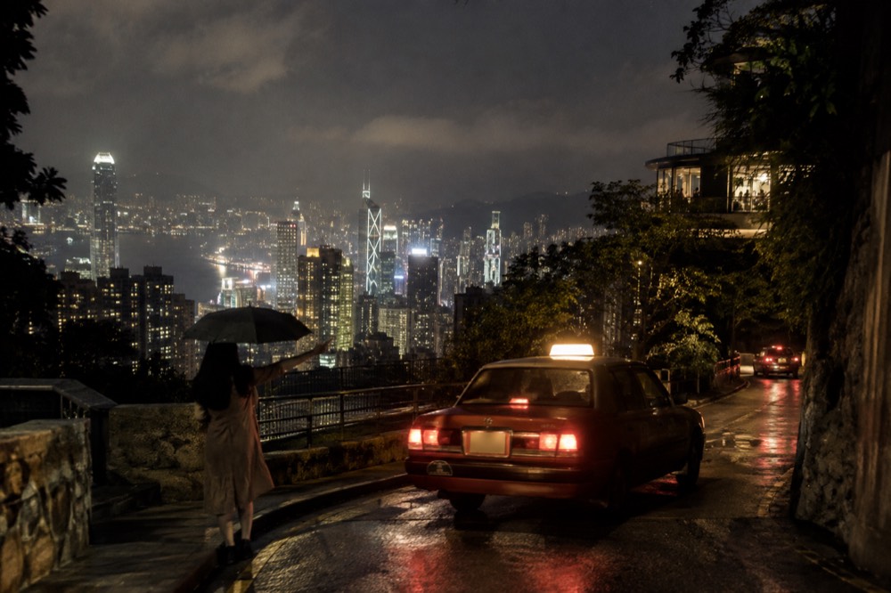 Red Hong Kong taxi on a narrow road above Central with the skyline behind
