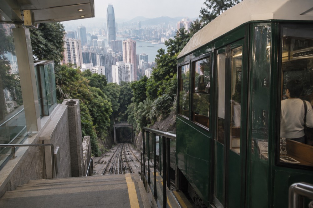 Green funicular tramcar at a hillside station platform with the city visible behind