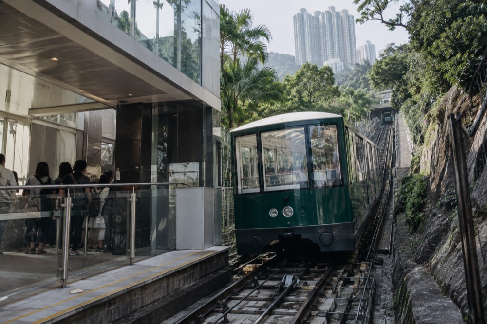 Modern green Peak Tram car with large panoramic windows departing the rebuilt lower terminus
