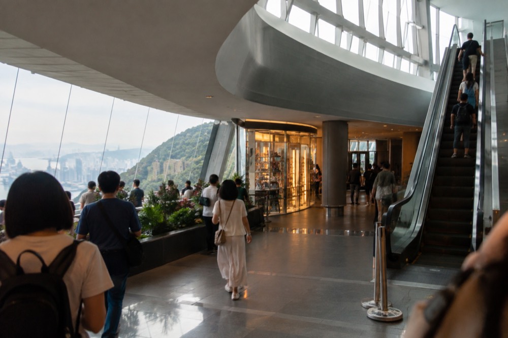 Crowd of visitors walking past shops inside the Peak Tower atrium in daytime
