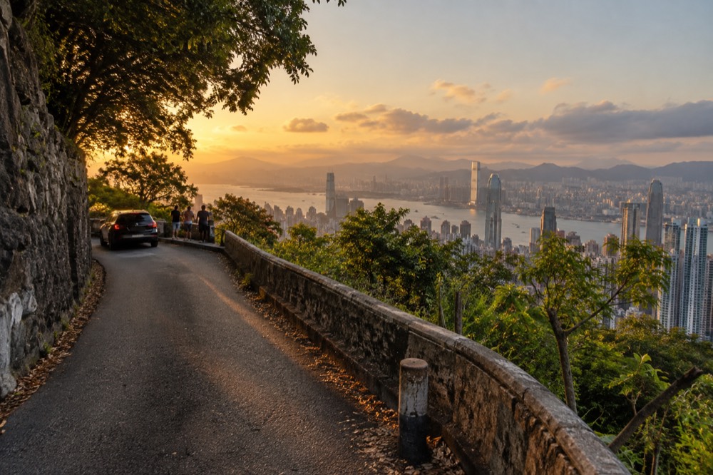 A flat narrow road winding along a green hillside above the harbour skyline